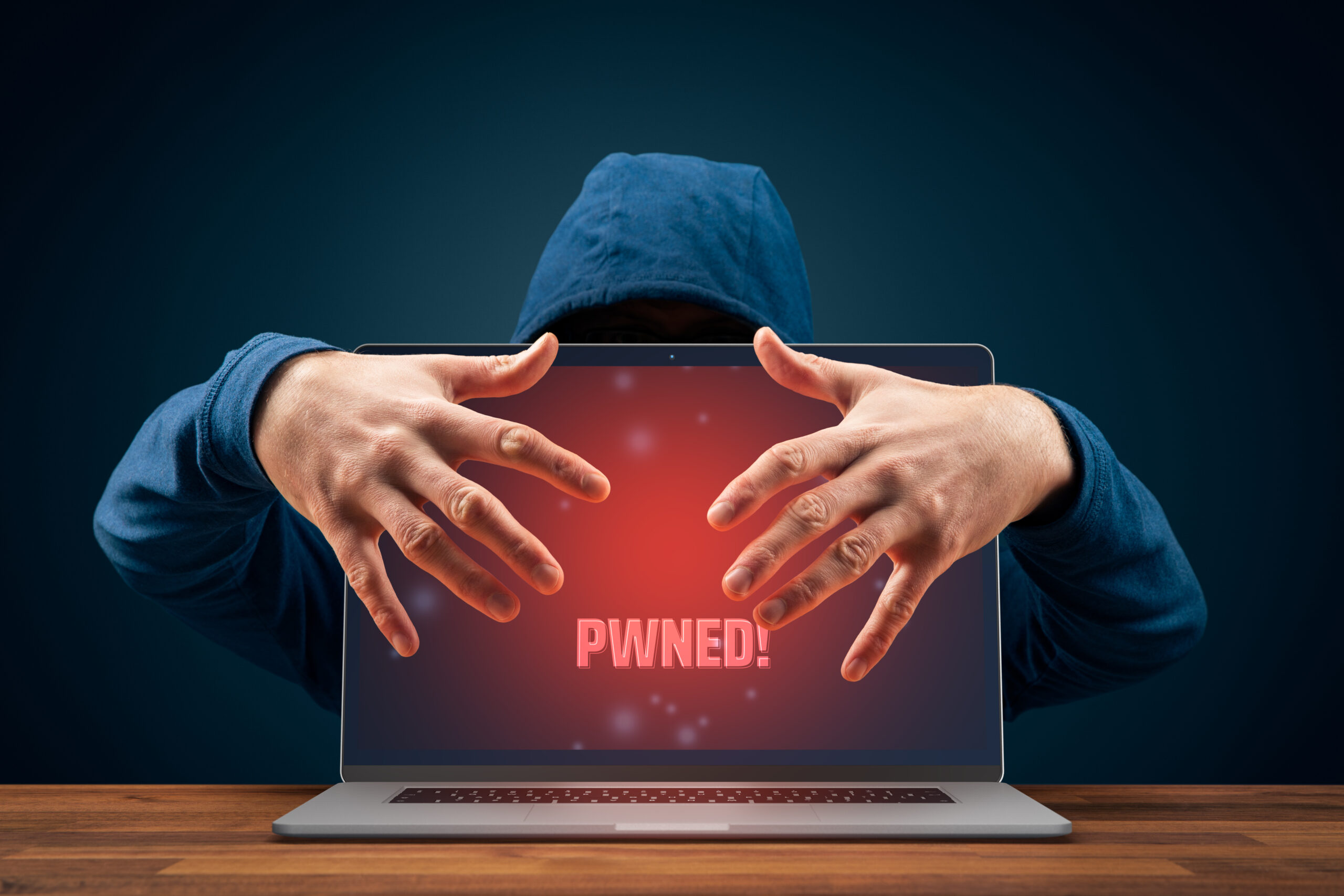 A hacker hovers behind a laptop with a red screen that says "Pwned"